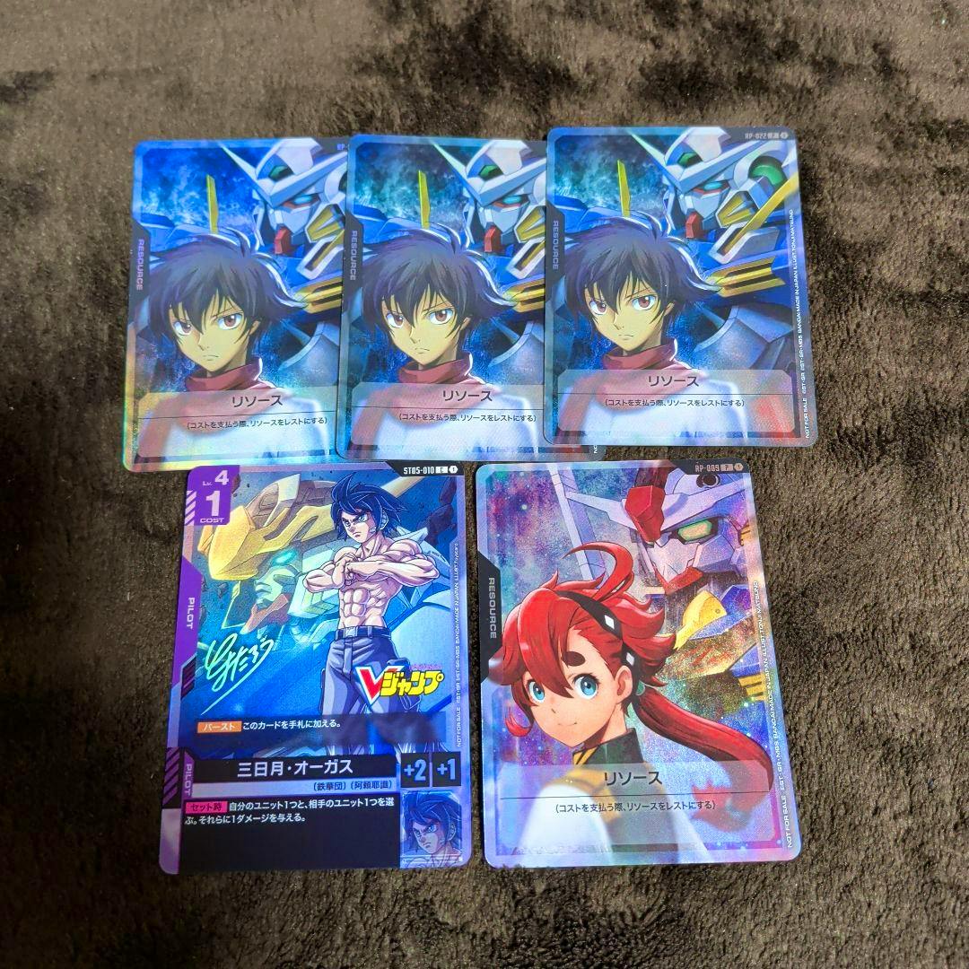 Photo of five Gundam trading cards from a V Jump supplement arranged on a dark fabric surface.