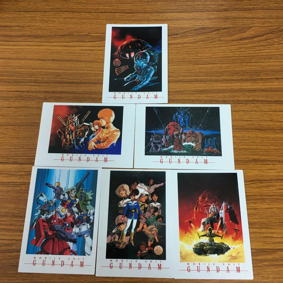 Seven Gundam photocards arranged in a pyramid layout on a wooden tabletop.