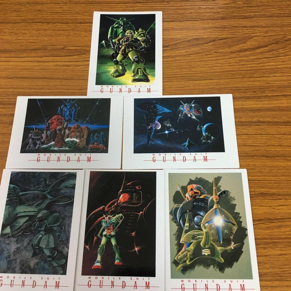 Photo of multiple Mobile Suit Gundam printed cards laid out on a wooden table.