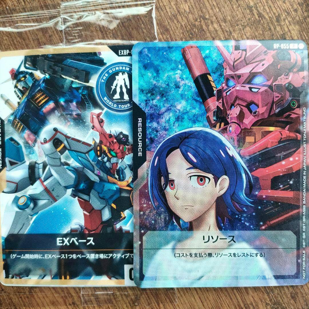 Two Gundam trading cards, one labeled EXベース and one labeled リソース, photographed overlapping on a wooden surface.