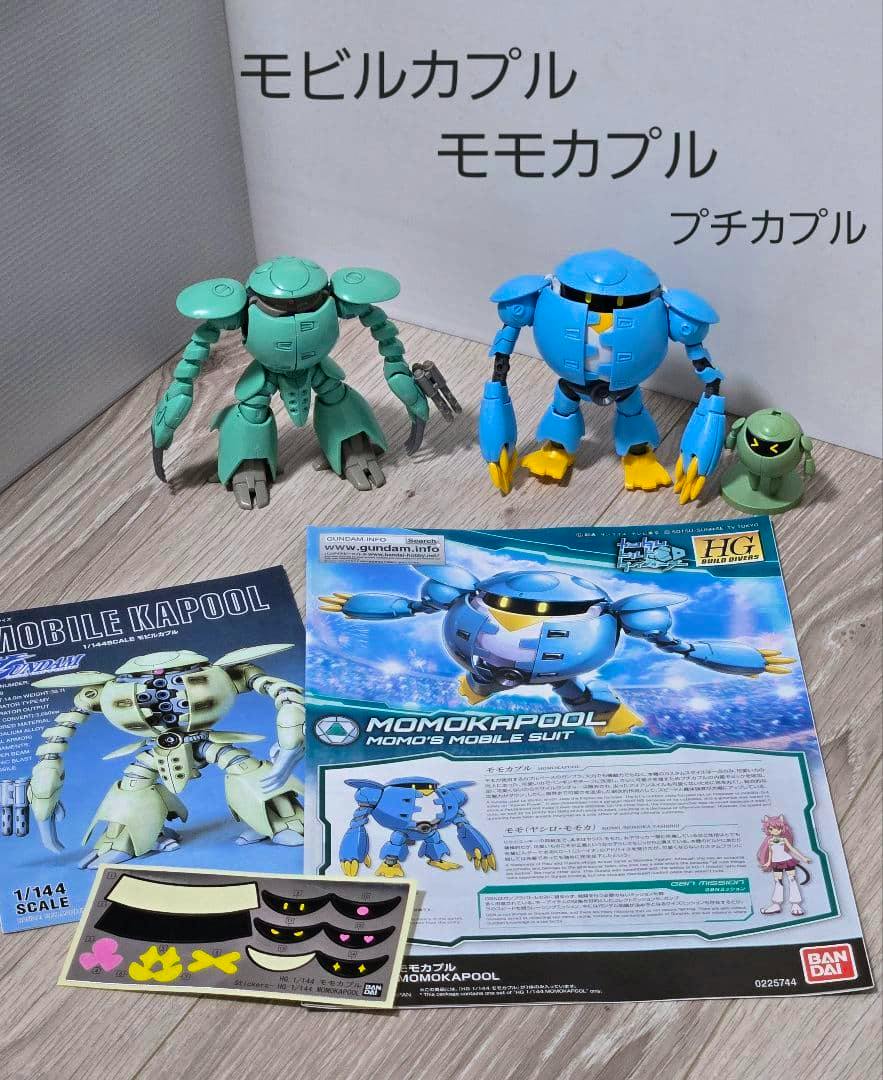 Two assembled 1/144 scale Mobile Kapool and Momokapool model figures with a smaller figure, instruction manuals, and a sticker sheet arranged on a tabletop.