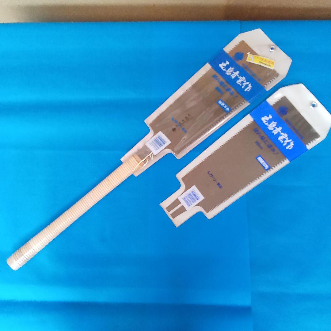 A handsaw with a wooden handle and two replacement saw blades in their packaging on a blue background.