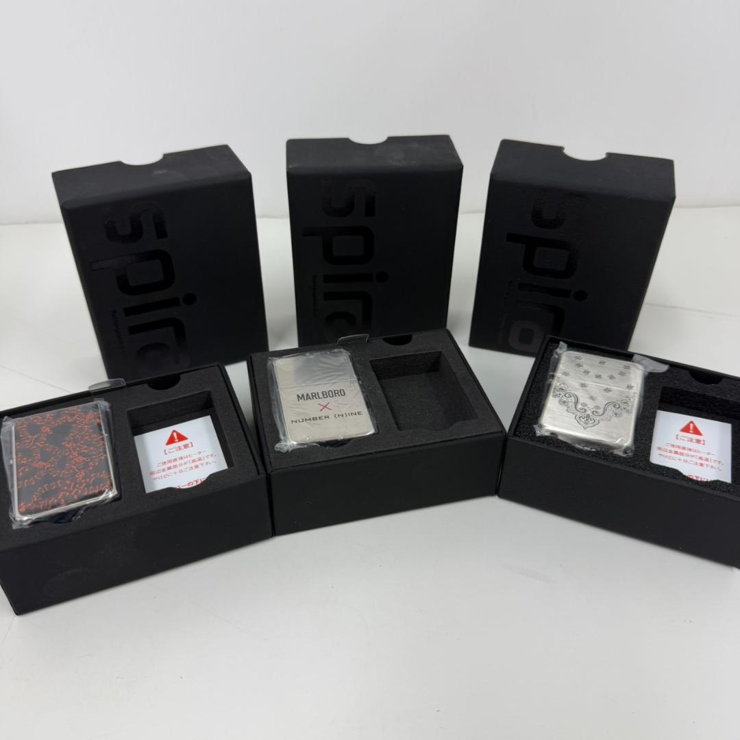 Three silver Zippo-style lighter cases shown in their black presentation boxes on a white surface.