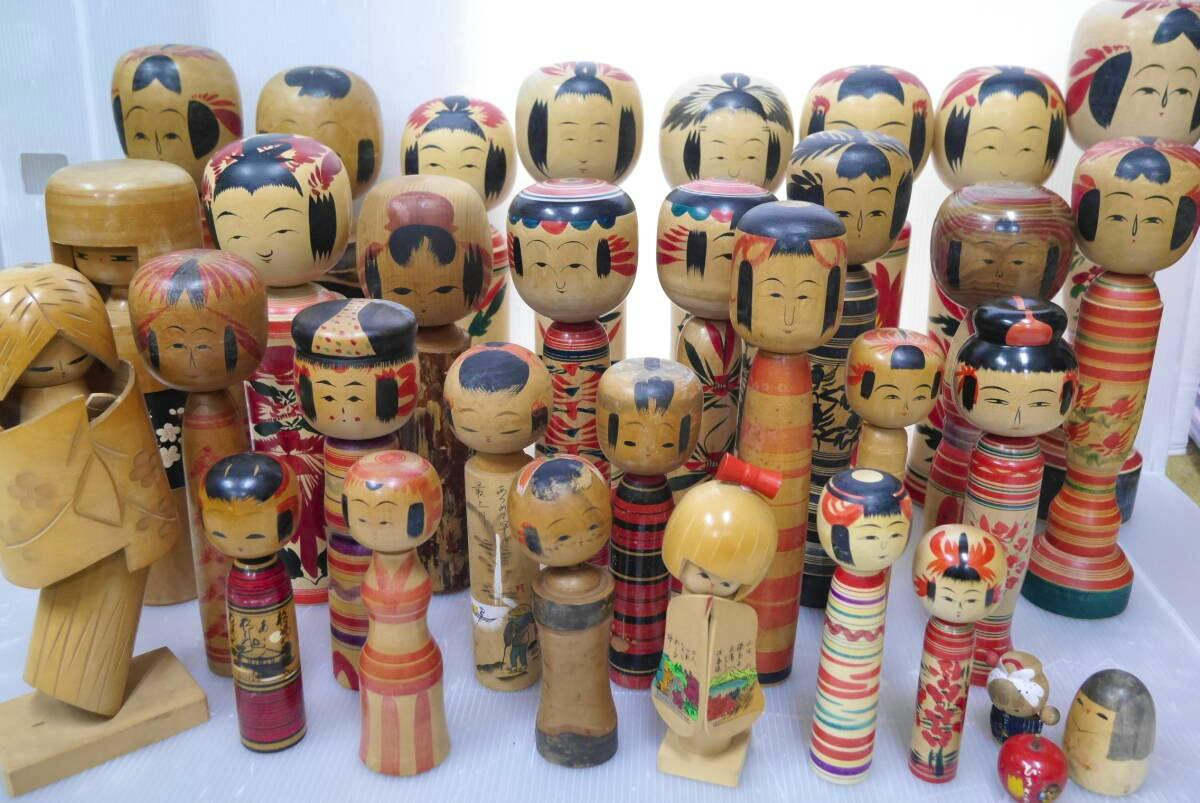 A large assortment of wooden kokeshi dolls of various sizes with painted faces and striped bodies arranged together on a surface.
