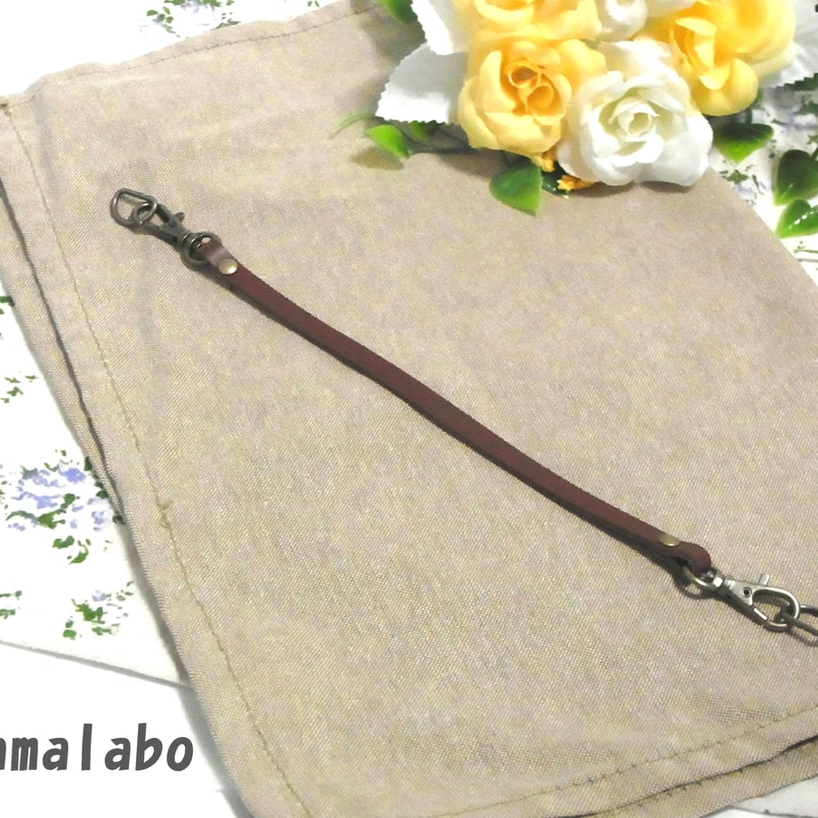 Brown 23cm cow leather strap keychain with antique metal clasps laid flat on fabric.