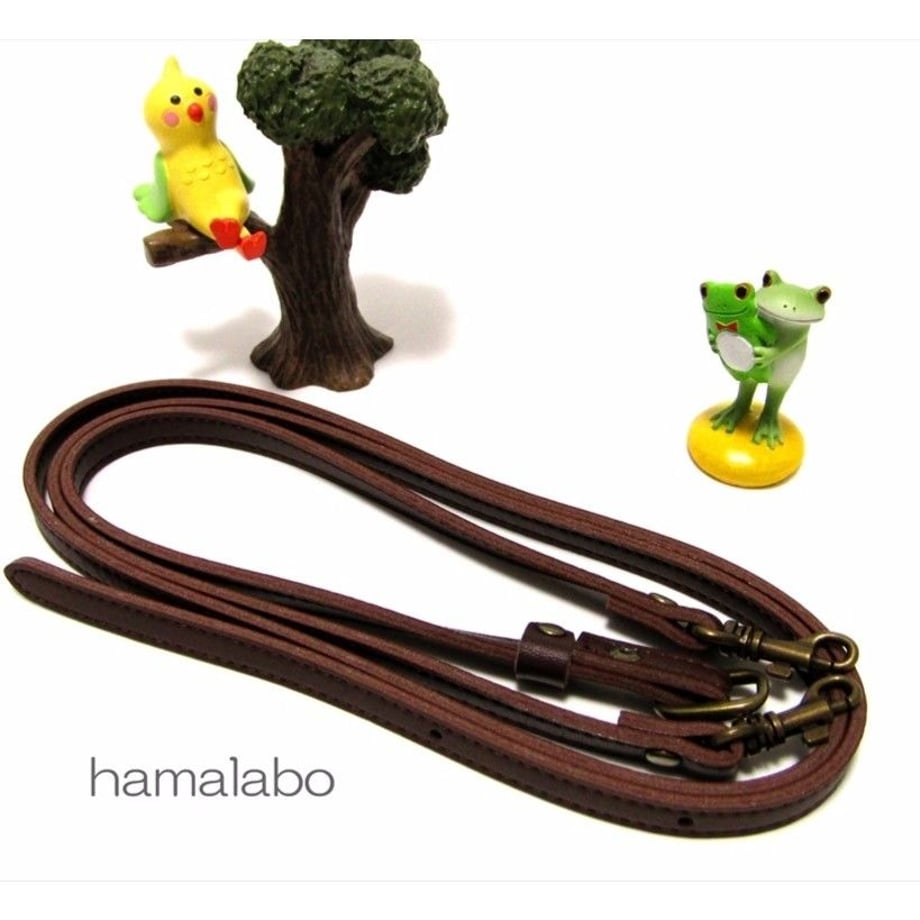 Brown adjustable cow-leather shoulder strap for a bag with antique brass-colored clasps, shown coiled on a white background.
