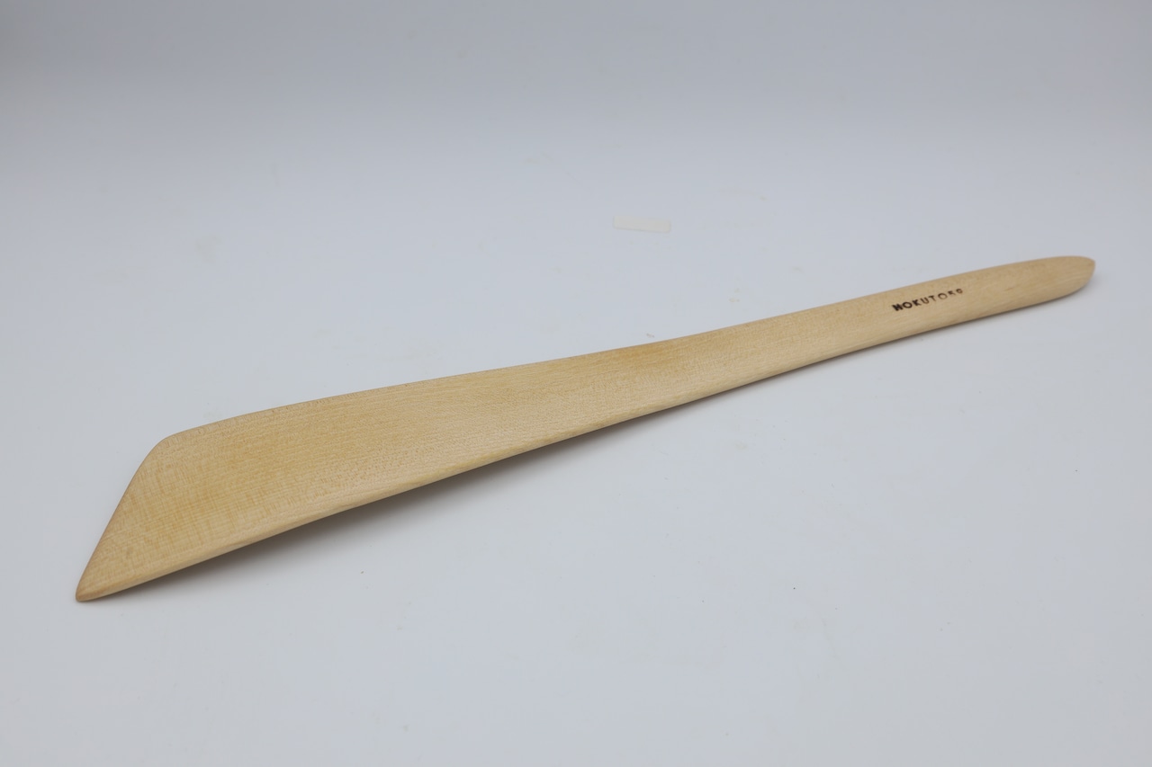 Wooden turner (spatula) shown on a plain light background photographed diagonally with a visible handle marking.