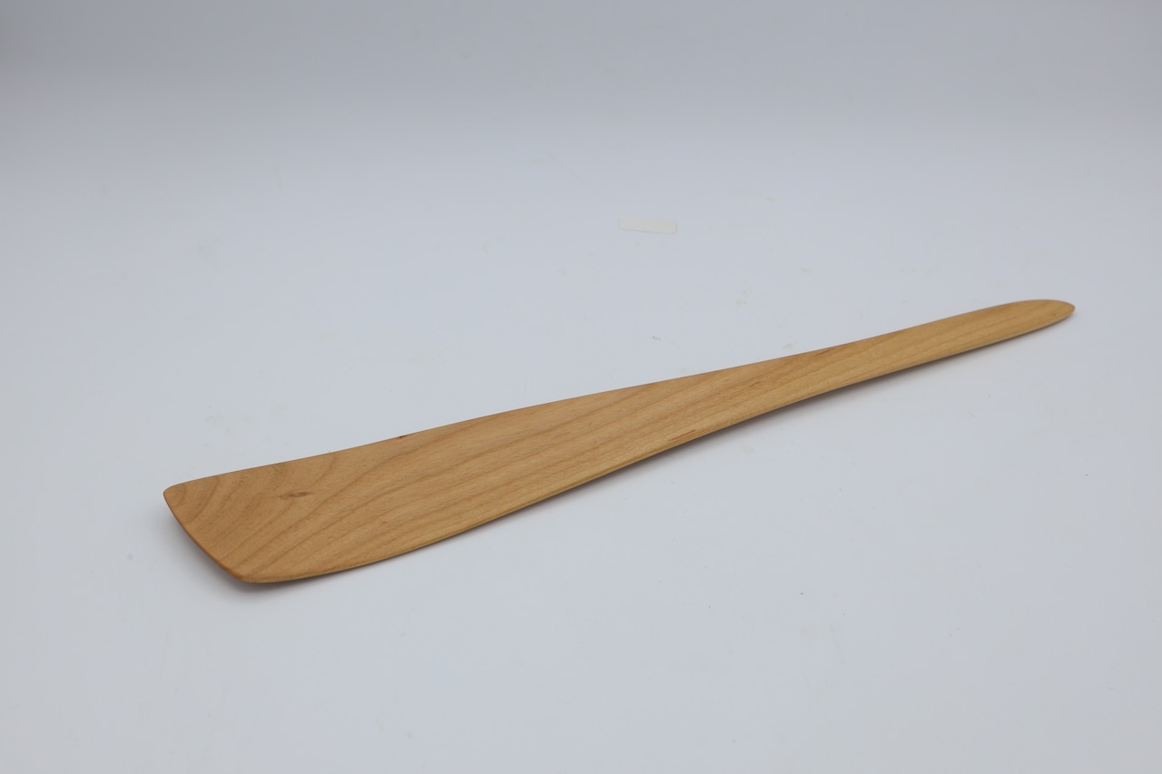 A wooden turner (spatula) laid flat on a plain light background, showing the full shape and flat blade.