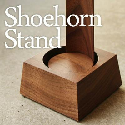 A wooden shoehorn stand holding a wooden shoehorn on a neutral surface, with the words "Shoehorn Stand" overlaid.