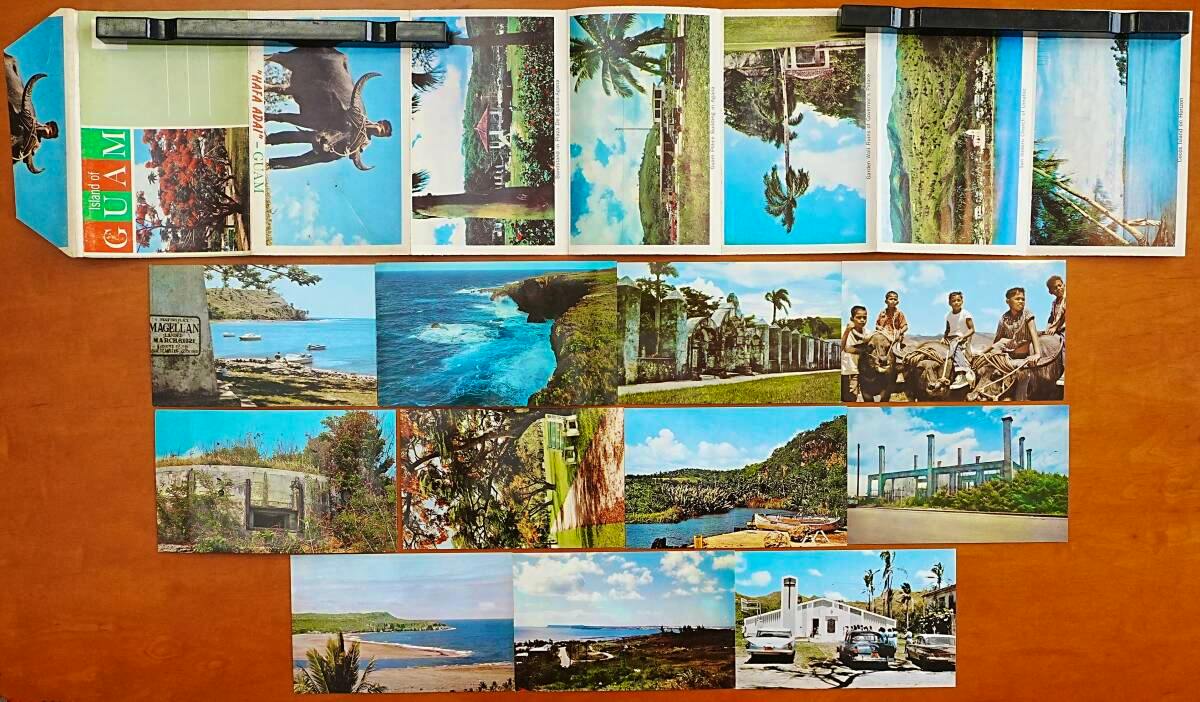 A spread of Guam postcards and a postcard folder laid out on a wooden surface.