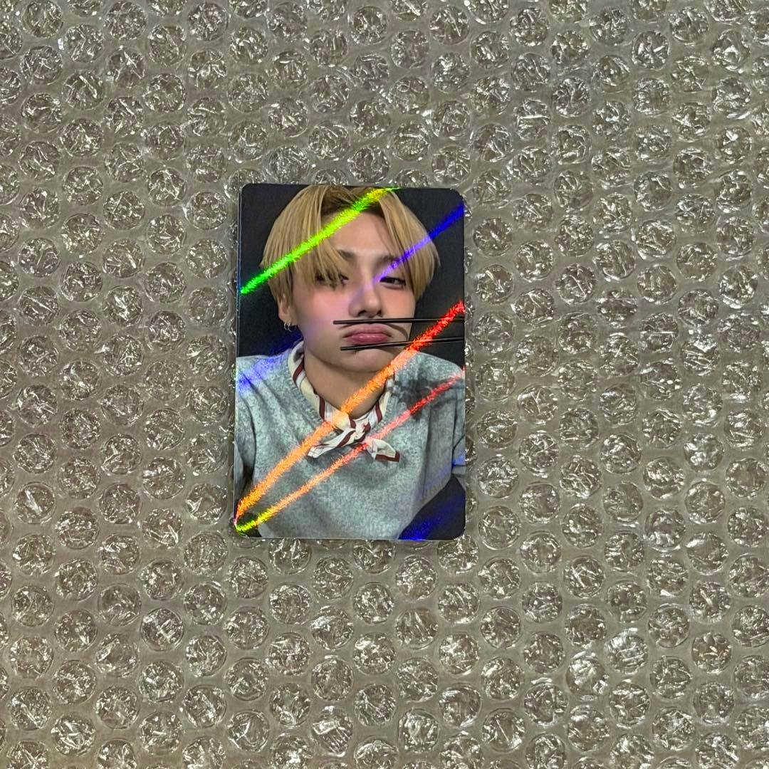 Holographic photocard front showing Sanwon with blonde hair making a pout, placed on bubble wrap.
