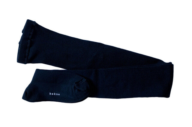A pair of dark merino wool rib tights laid flat on a white background, showing the foot with a small hakne logo.