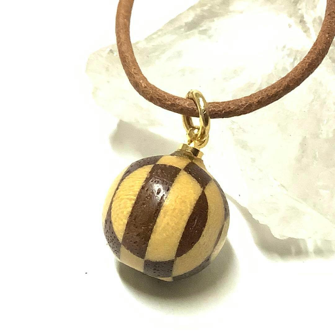 Close-up of a Hakone wooden yosegi temari ball pendant with alternating light and dark wood stripes hanging from a leather cord.