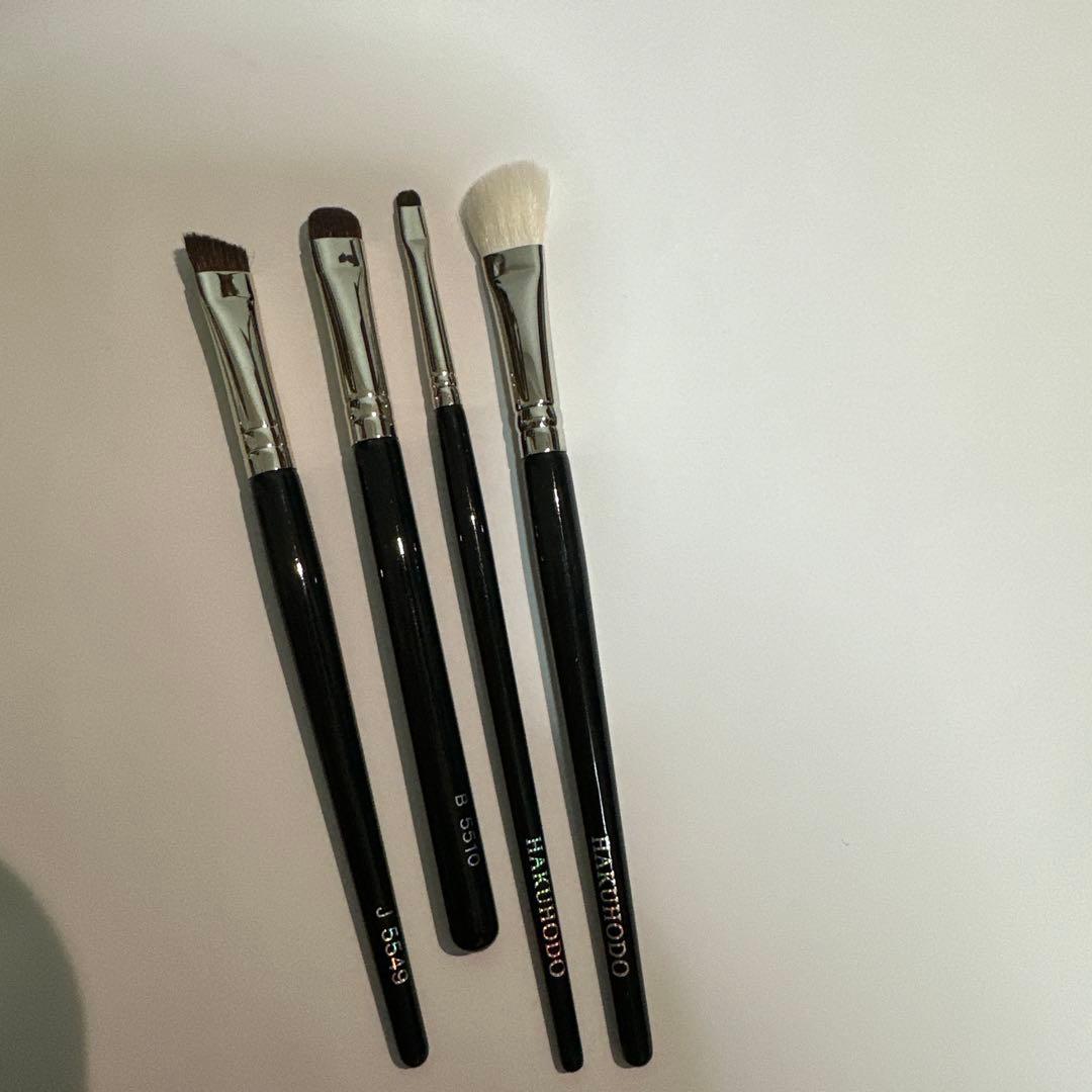 Four Hakuhodo eyeshadow brushes with black handles laid flat on a white background.