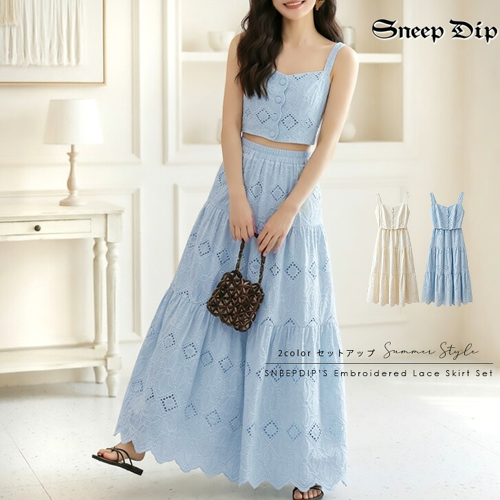 Model wearing a light blue embroidered lace sleeveless cropped top with a matching long tiered skirt, holding a small woven bag in a bright room.