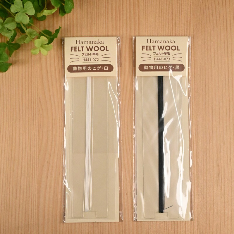 Two packaged Hamanaka FELT WOOL animal whisker strips, white (H441-072) and black (H441-073), displayed on a wooden surface.