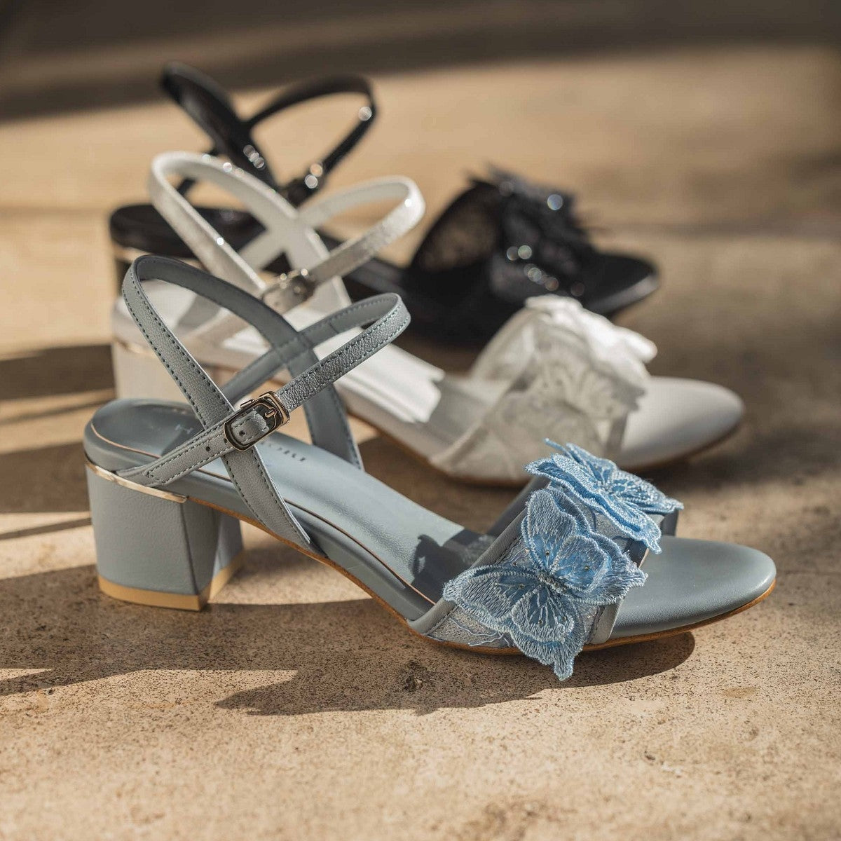Blue HANAE MORI×HIMIKO butterfly sandal in front with white and black pairs behind on a floor.