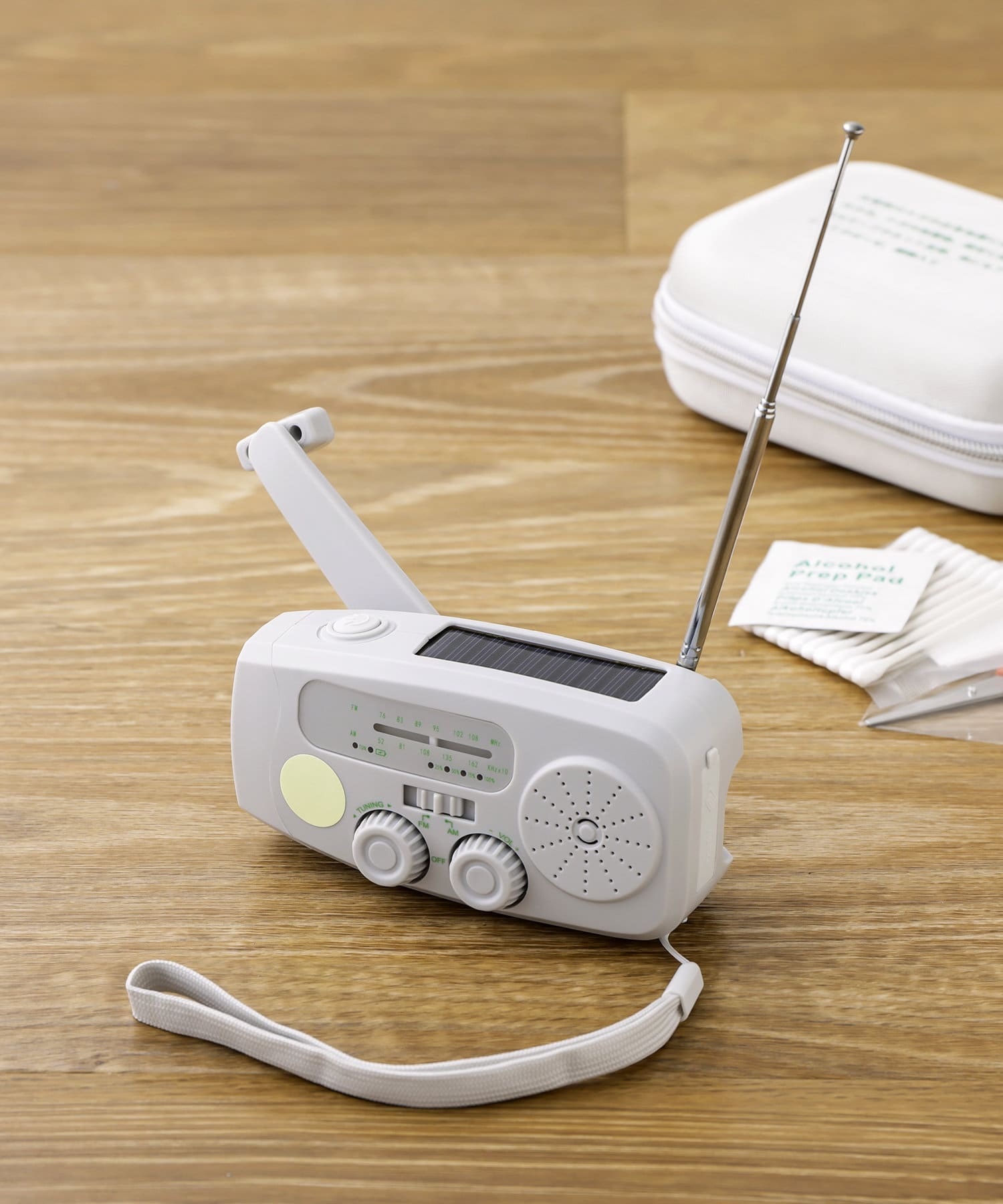 White hand-crank emergency radio with extended antenna, visible crank handle, and wrist strap on a wooden surface.