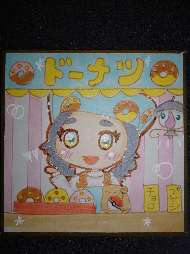 Photograph of a hand-drawn illustration of a Pokémon (Lampent) at a donut stand with colorful donuts and Japanese text.
