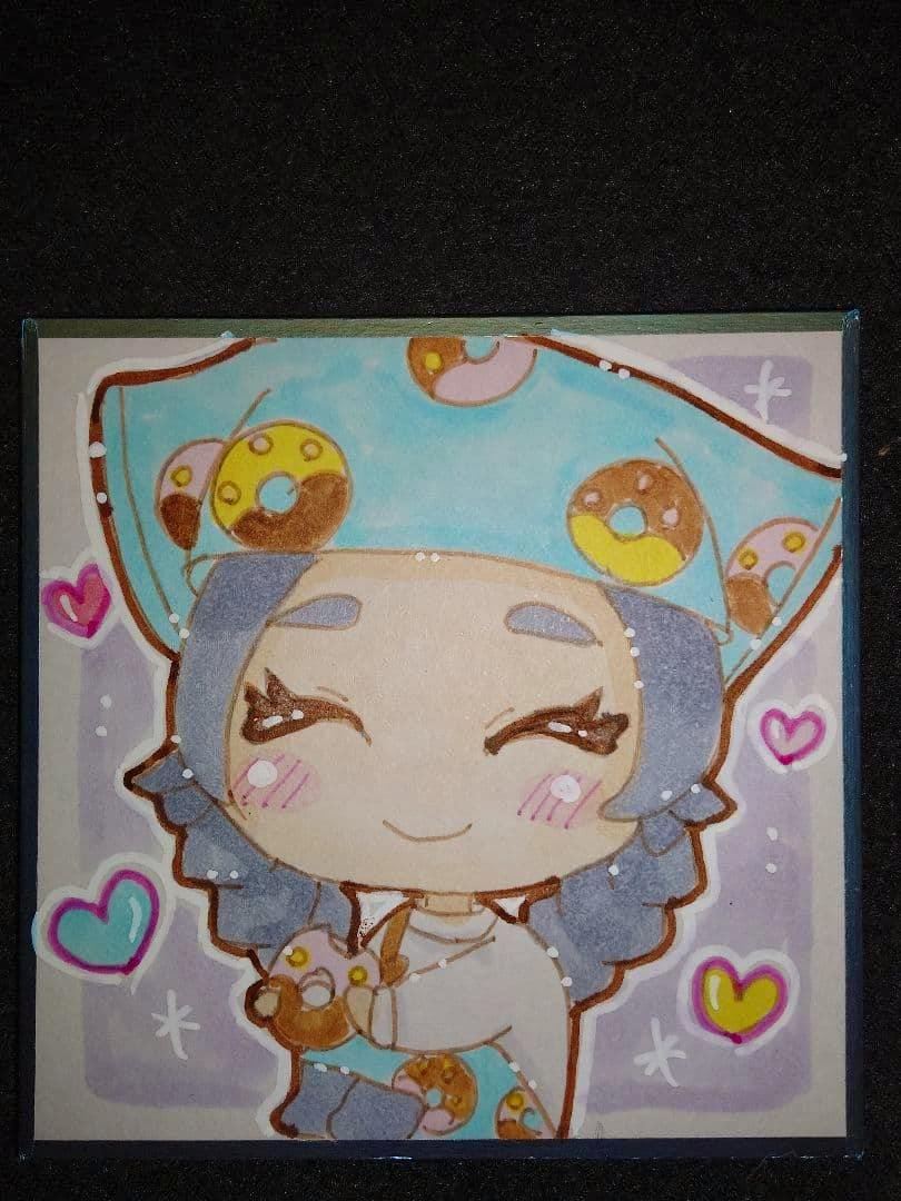 Square hand-drawn illustration on a picture board of a smiling chibi character wearing a blue donut-patterned hat and holding a small donut.