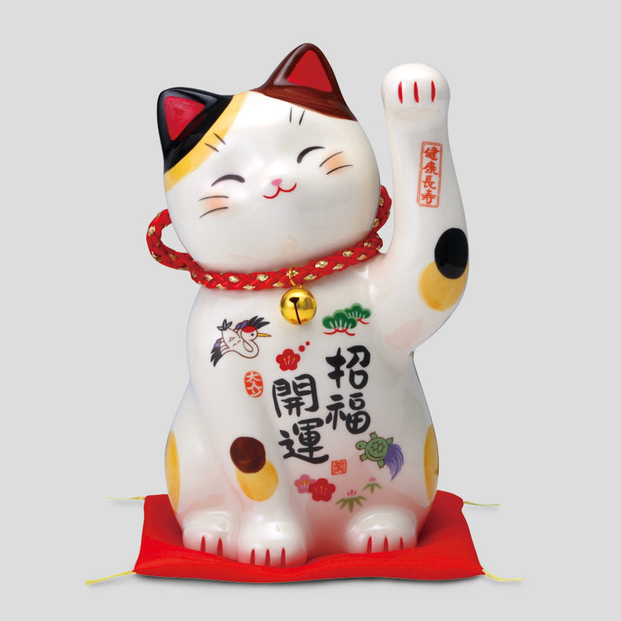 Front view of a painted ceramic beckoning cat figure with a red cord and bell, sitting on a red cushion.