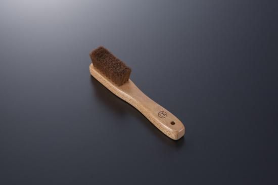 A wooden-handled suede shoe brush with brown bristles shown on a dark surface.