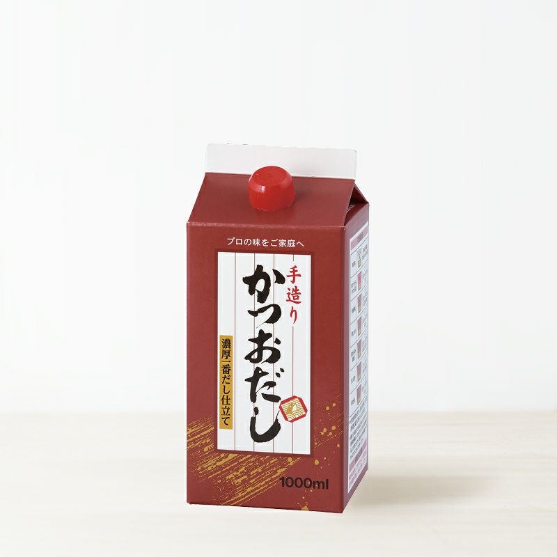 A 1000ml red carton of 手造りかつおだし (bonito dashi) with a red screw cap on a light background.