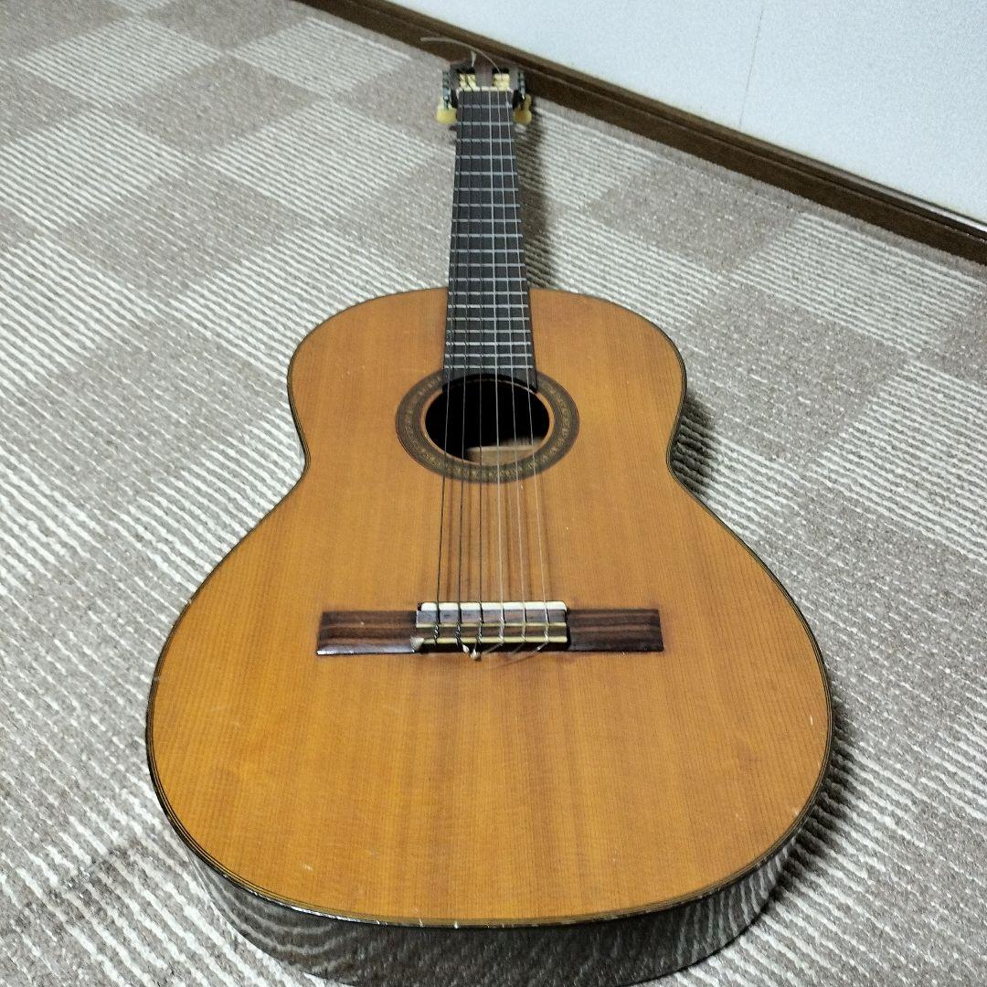 Top-down view of the classical guitar showing its soundboard, bridge, strings, and neck while lying on a carpeted floor.