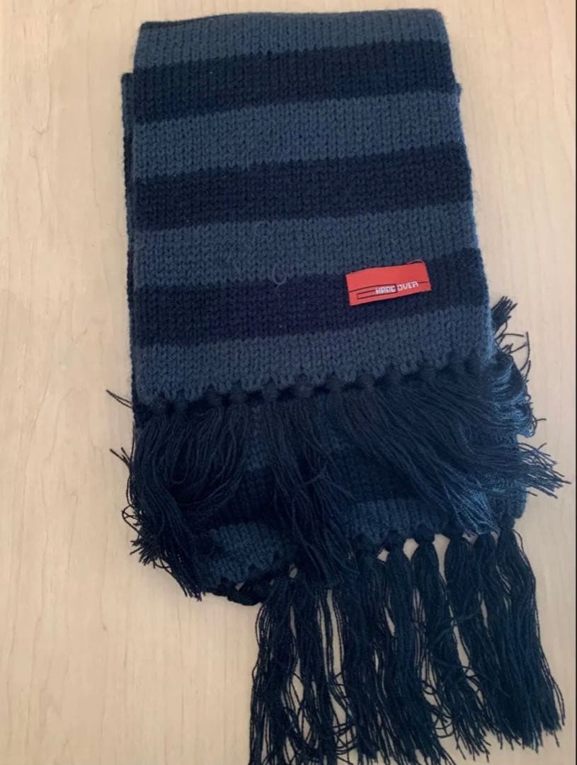 Folded striped polyester scarf with fringed ends and a red label on a wooden surface.