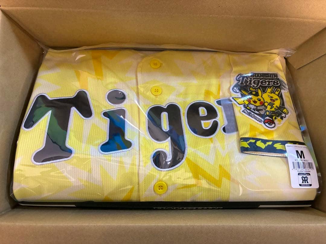 Folded unopened yellow Hanshin Tigers limited Pokémon design uniform in plastic packaging inside a cardboard box with size M tag visible.