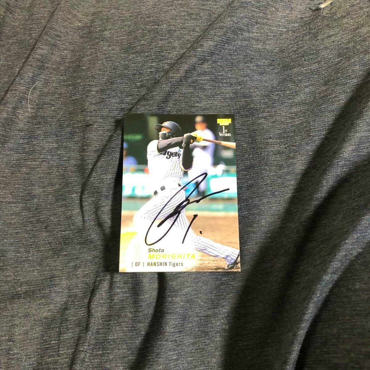 A photo of a Hanshin Tigers trading card for Shota Morishita with a large black autograph, placed on a gray fabric background.
