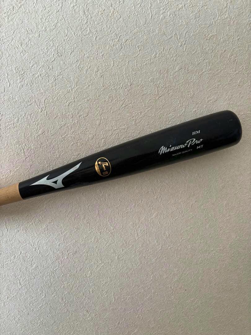 A black Mizuno Pro baseball bat showing the barrel, handle, and logos against a textured wall.