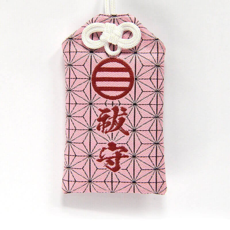 Pink cloth amulet with hemp-leaf (asanoha) pattern, red embroidered characters, and a white cord.