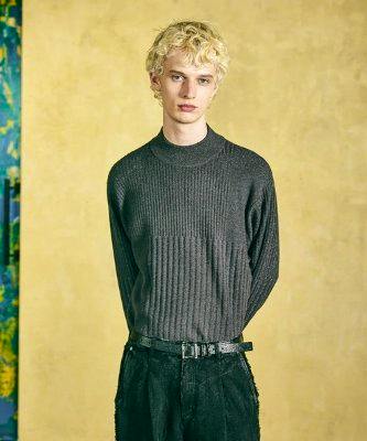 Person wearing the high-neck sweater shown from the front against a yellow background.