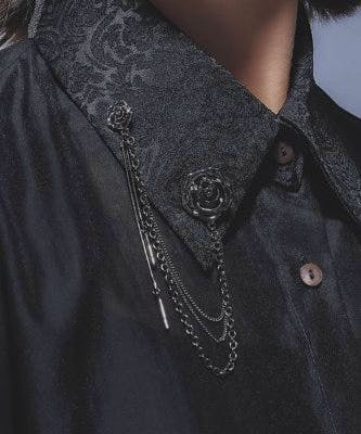 Motif chain metal brooch pinned to a black shirt collar with decorative dangling chains.