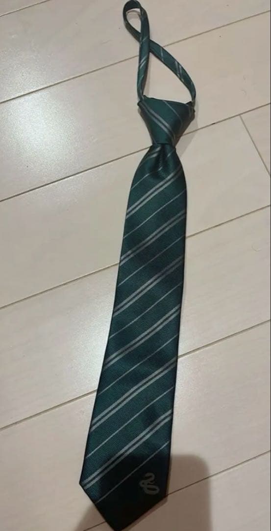 Green Slytherin striped polyester necktie laid flat on a light wood floor with a loosely tied knot.