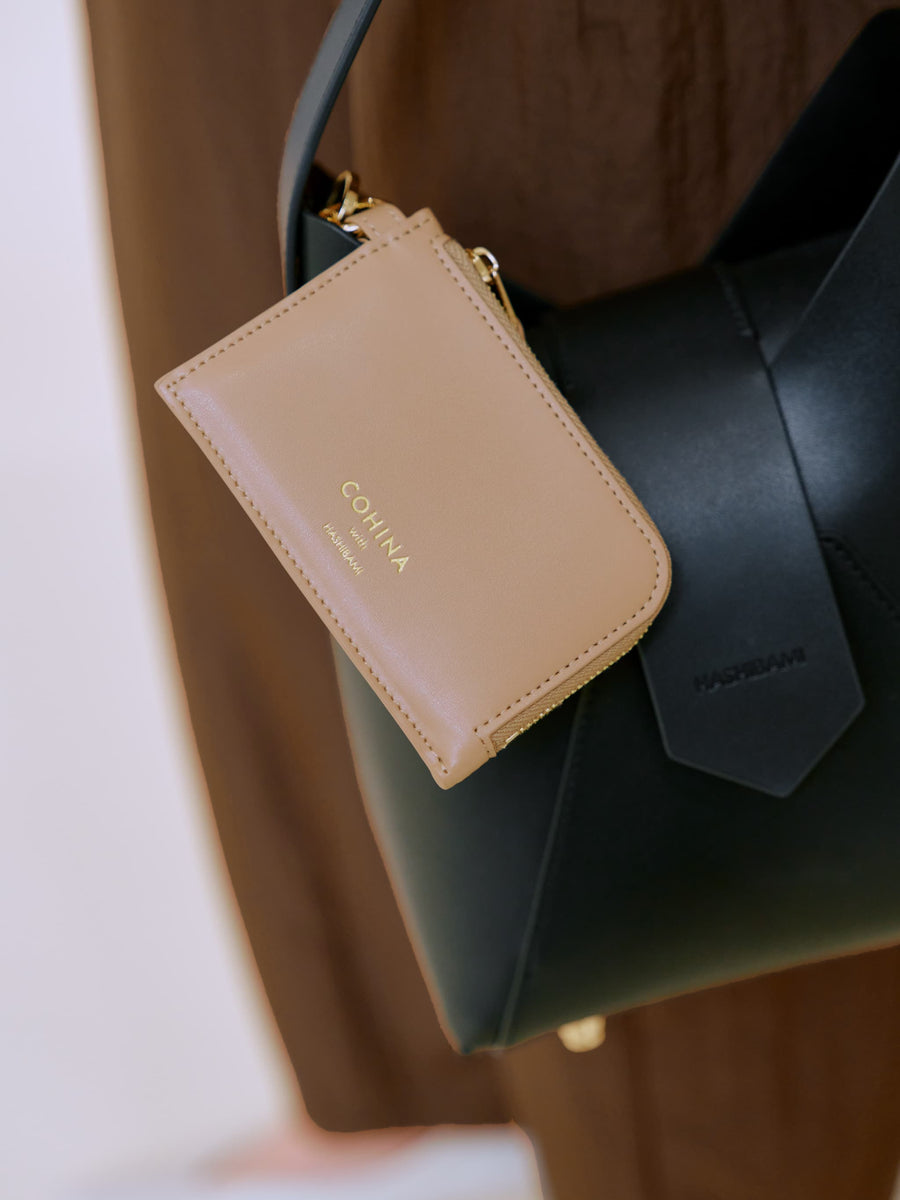 Beige small leather fragment case with gold hardware attached to a black handbag.