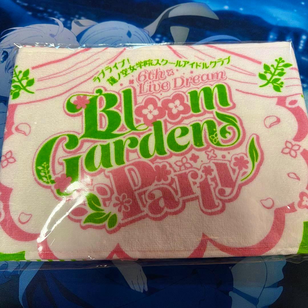 Folded Bloom Garden Party muffler towel showing pink and green printed logo, in plastic packaging.