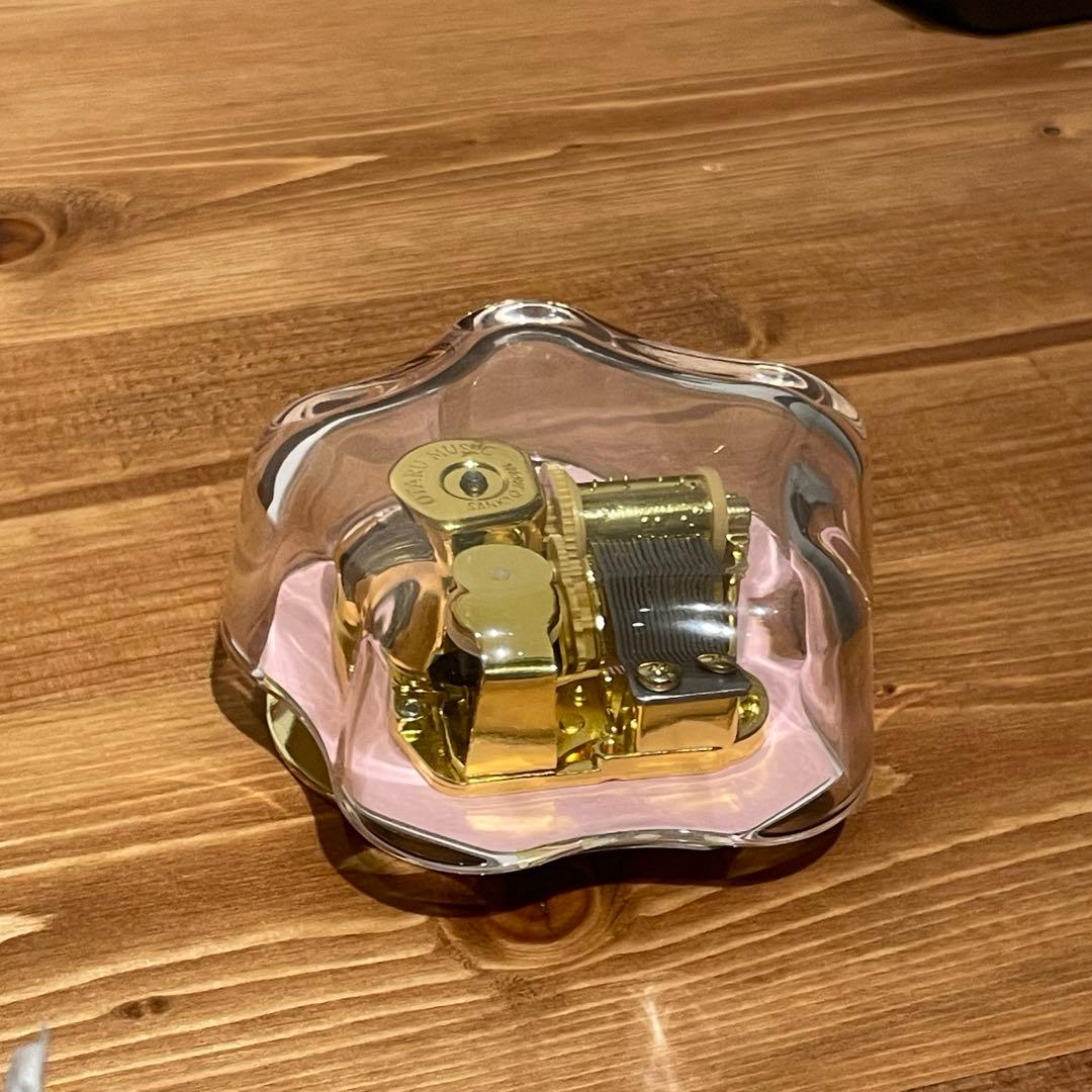 Flower-shaped clear glass music box showing the gold-tone music mechanism inside, on a wooden surface.
