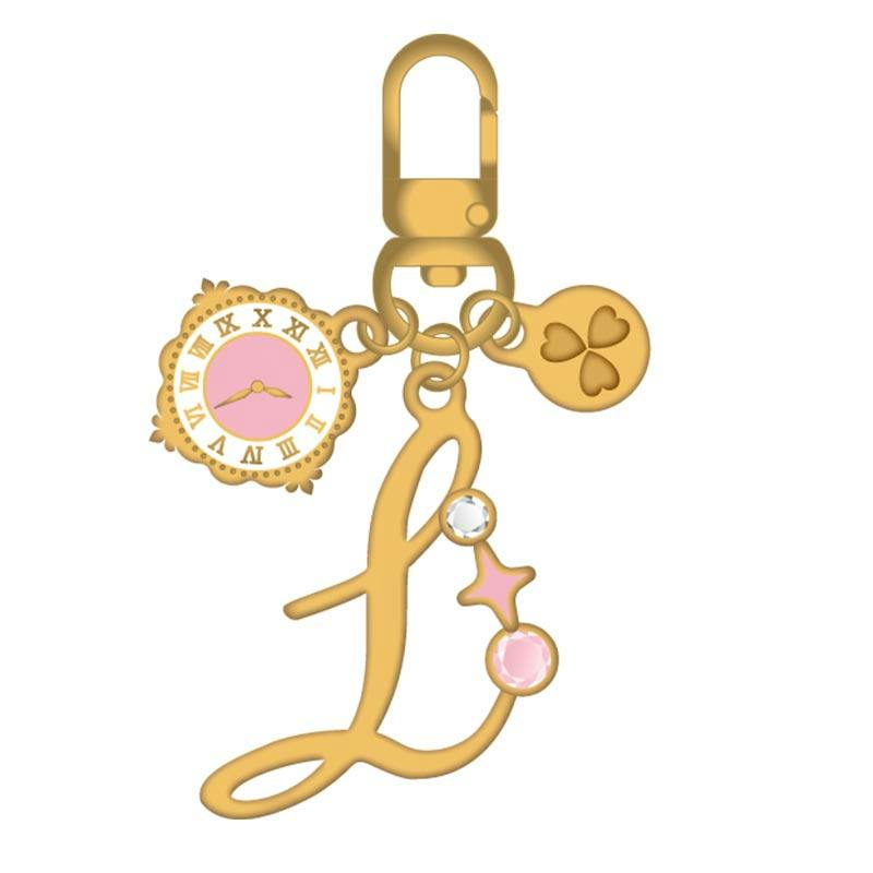 Illustration of the acrylic keychain showing a gold-colored letter "L" pendant with small clock and clover charms.