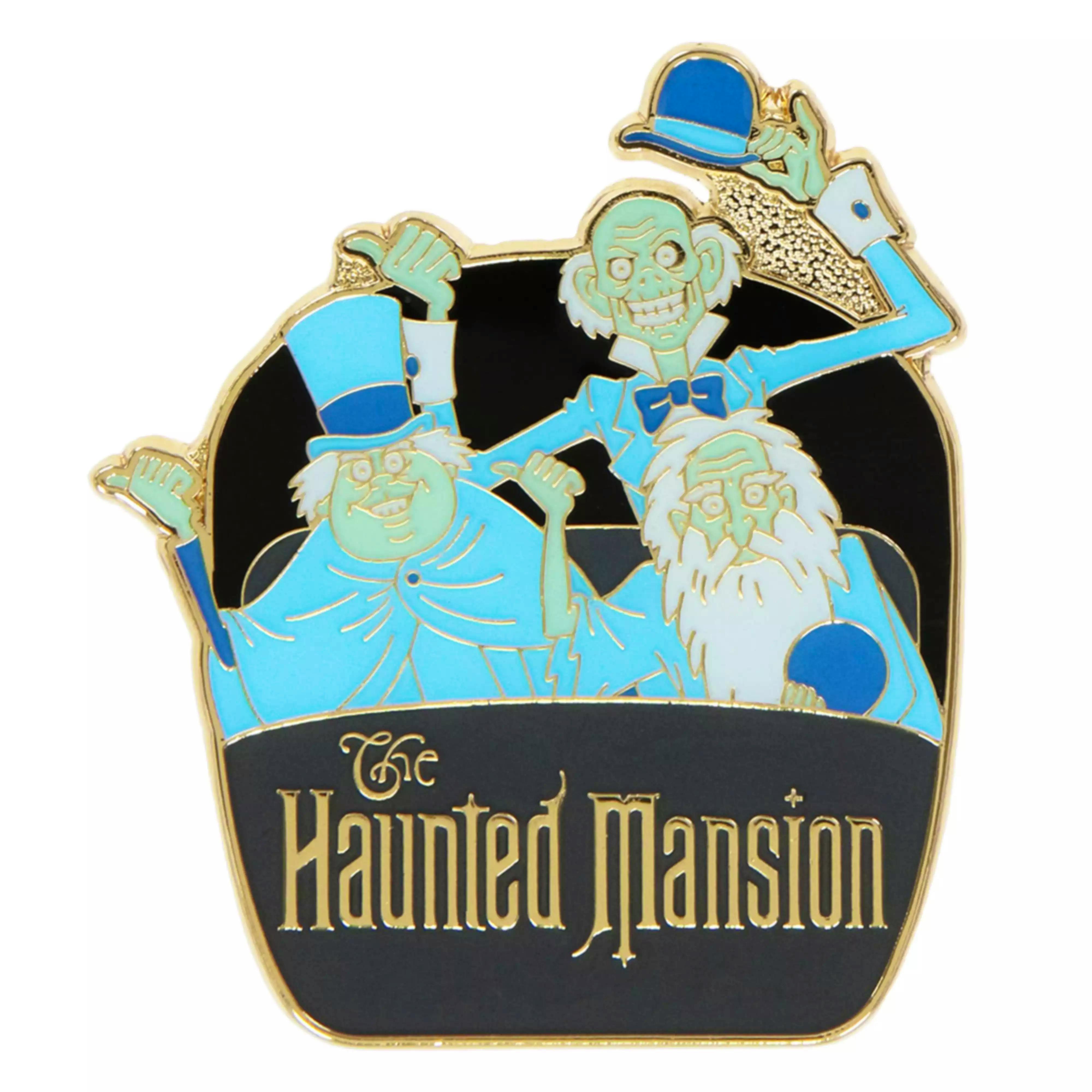 Close-up photo of a Haunted Mansion pin badge showing three blue-green ghosts and the word "Haunted Mansion" on a black background.