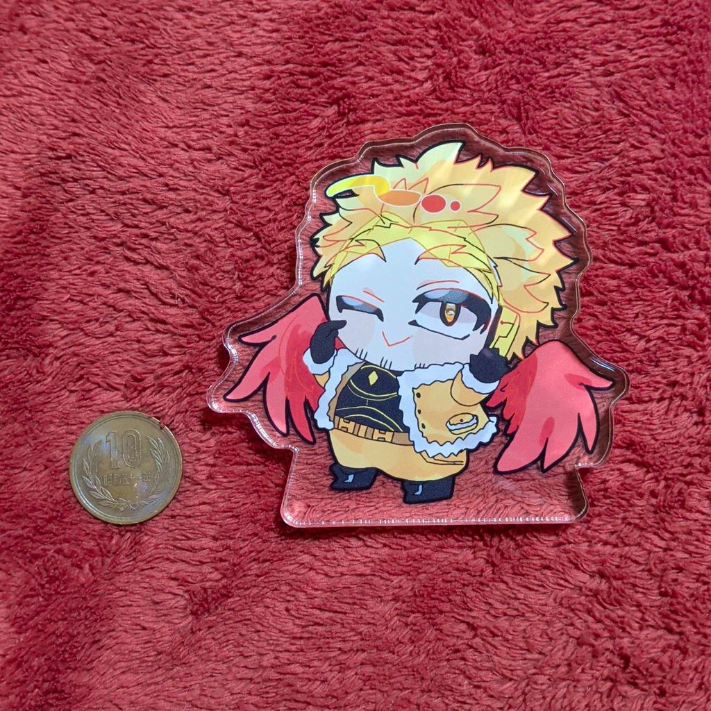 A Hawks acrylic block featuring a chibi character with yellow hair and red wings on a red textured cloth next to a 10-yen coin.