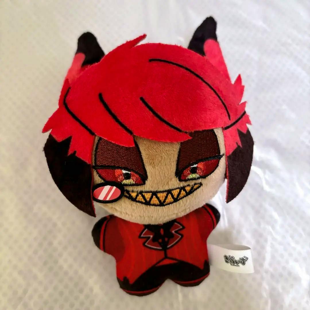 Front view of the Hazbin Hotel Alastor plush showing red hair, embroidered eyes and a toothy stitched grin with a fabric tag.
