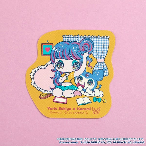 Die-cut Yurie Sekiya × Kuromi collaboration sticker showing an illustrated girl with Kuromi on a yellow-shaped background photographed on pink paper.