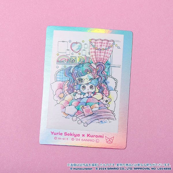 Holographic Yurie Sekiya × Kuromi sticker showing a pastel illustration of Kuromi nestled among cushions on a pink background.