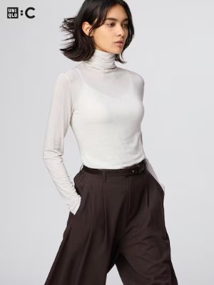 A model wearing the listed light-colored long-sleeve knit top with dark trousers.