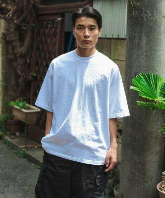 Person wearing a plain white HEAVYWEIGHT COLLECTIONS standard T-shirt standing outdoors.