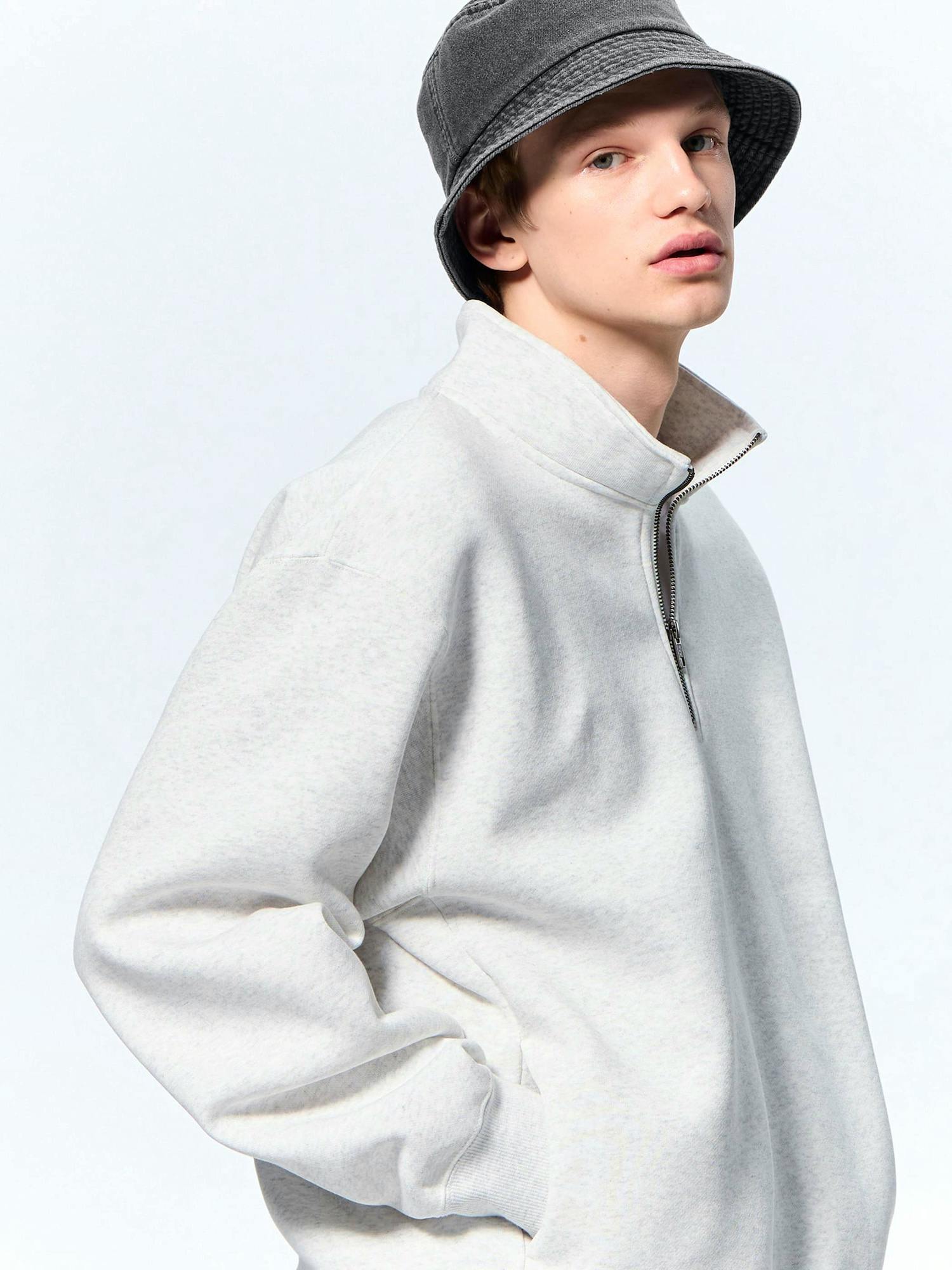 Model wearing the heavy-weight half-zip pullover in light gray with the zipper partially open and hands in pockets.