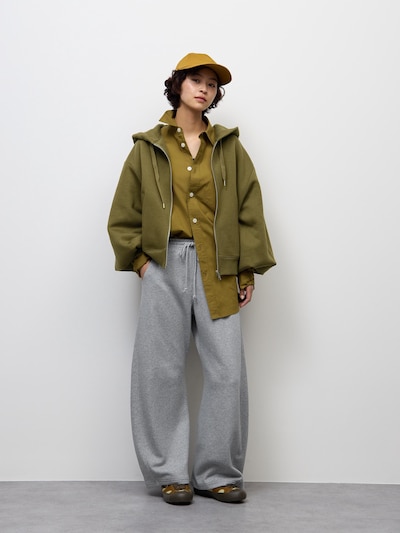 Model wearing grey barrel-leg sweatpants paired with an olive jacket and cap against a white background.