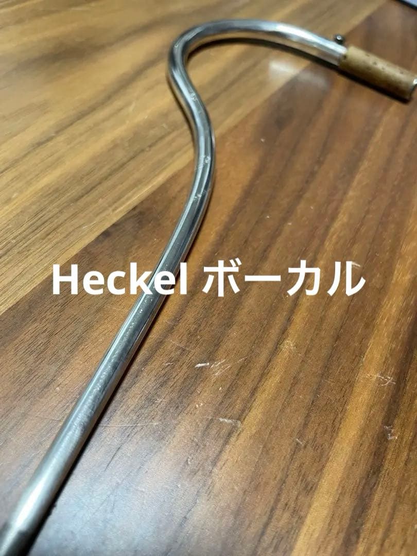 Curved metal Heckel bassoon bocal mouthpiece on a wooden surface.